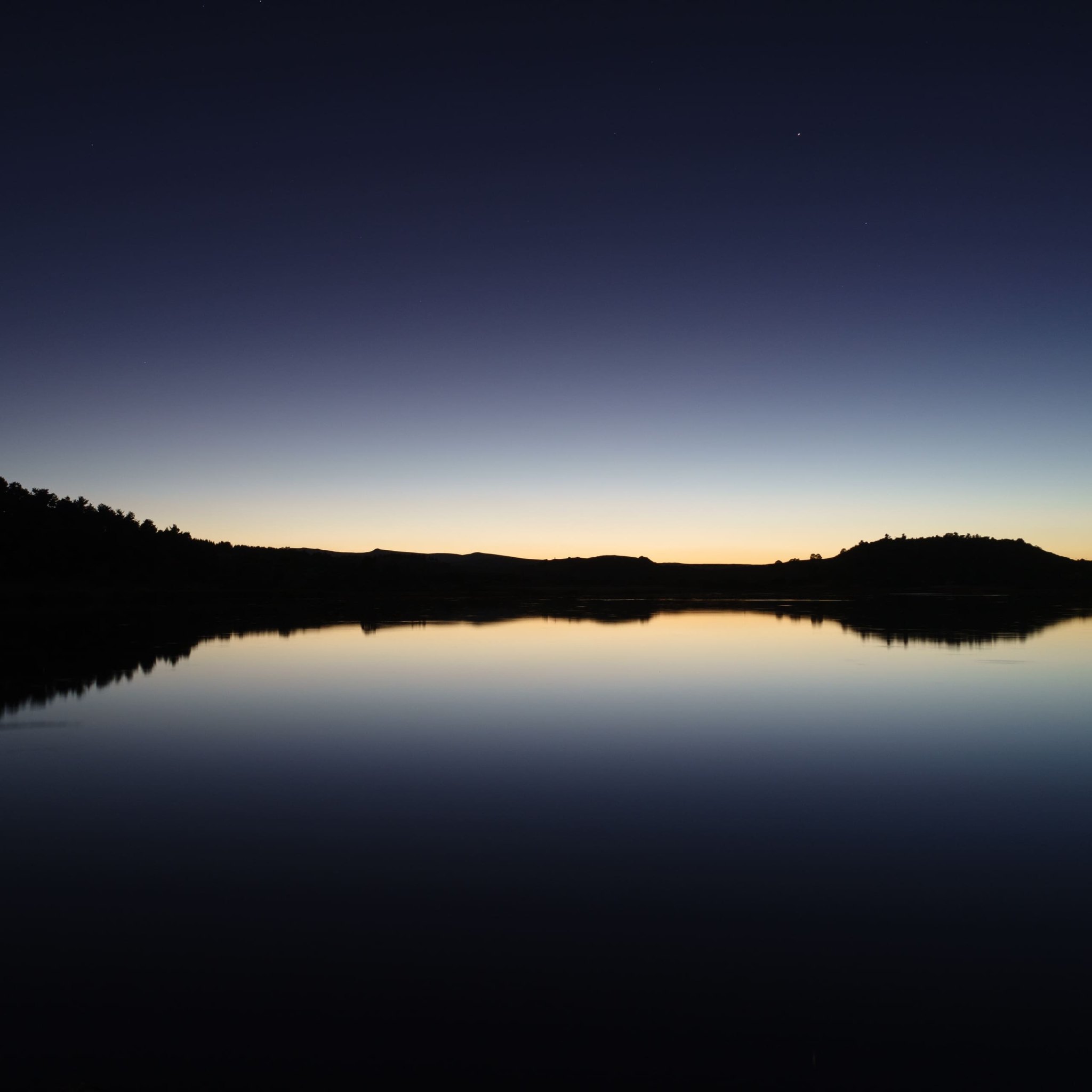 Le lac du Pêcher au crépuscule, les reliefs en silhouette se reflètent dans une eau parfaitement immobile, sous un dégradé bleu nuit vers l'ambre où brille une étoile.