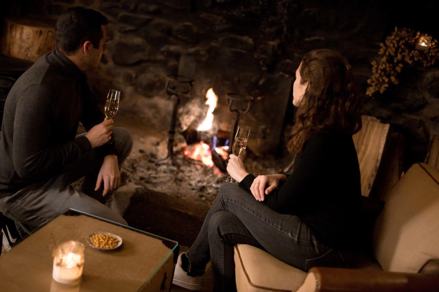 Couple au coin du feu de Cantou à l'Ecolodge instants d'Absolu. Champagne pour célébrer Noël.