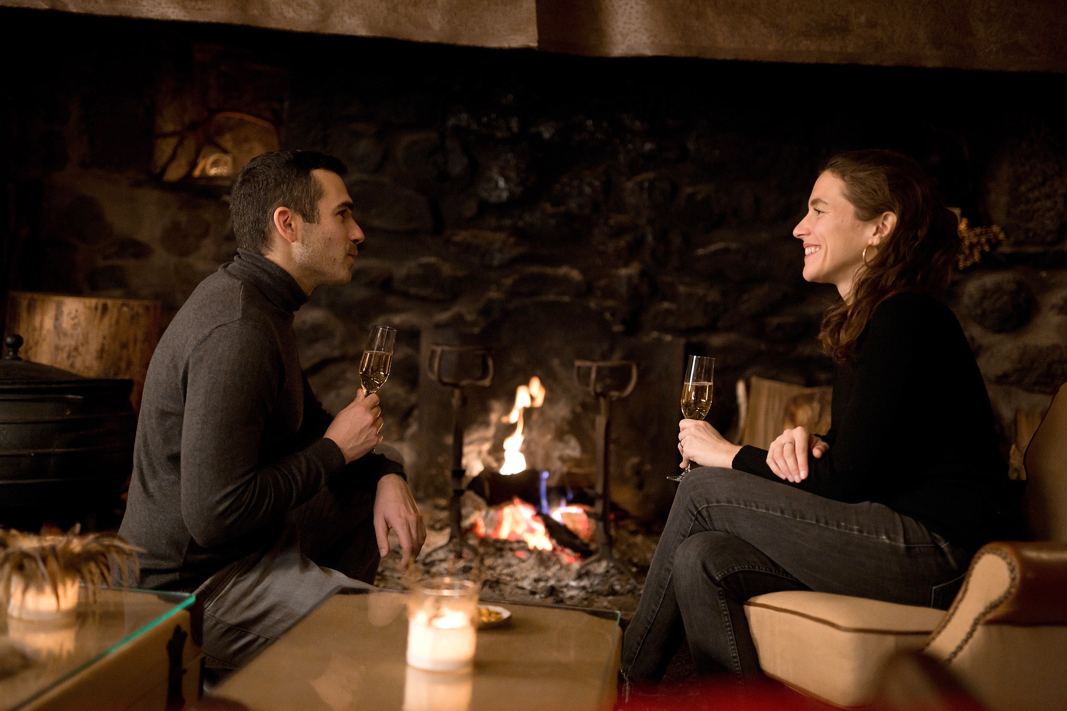 Couple enjoying a glass of champagne by the fireplace, celebrating their Christmas Break in the French Highlands at ecolodge instants d'Absolu.